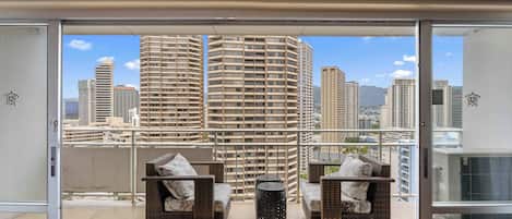 A balcony with wicker furniture, a round table, and a cityscape view.