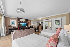 Ein Hotelzimmer mit zwei Betten, einer Sitzecke, einem Esstisch, einer Küchenzeile und Bildern an den Wänden.