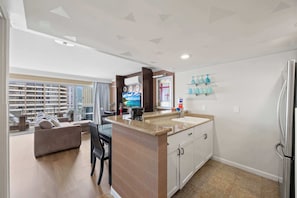 A modern kitchen with a central island, a dining area with a sofa and chairs, and a view of high-rise buildings. - @ Marbella Lane - Iconic Waikiki City View Getaway (Honolulu)