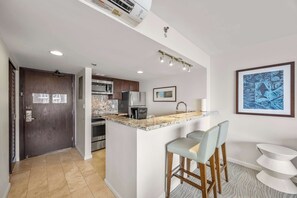 Una cocina moderna con una isla central, taburetes de bar, microondas y refrigerador.