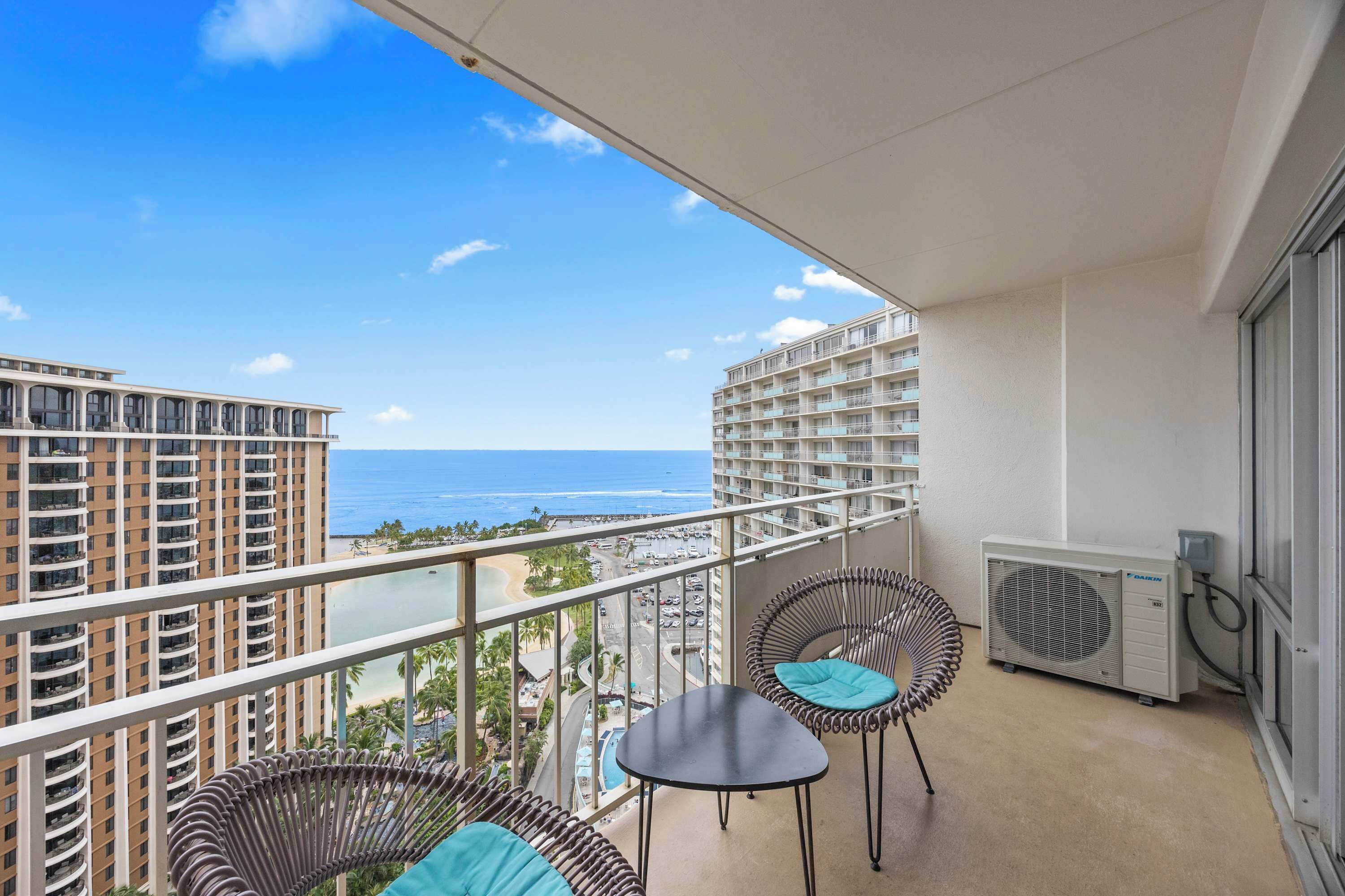 Ein Balkon mit Korbstühlen und einem Tisch, mit Blick auf Strand und Meer.