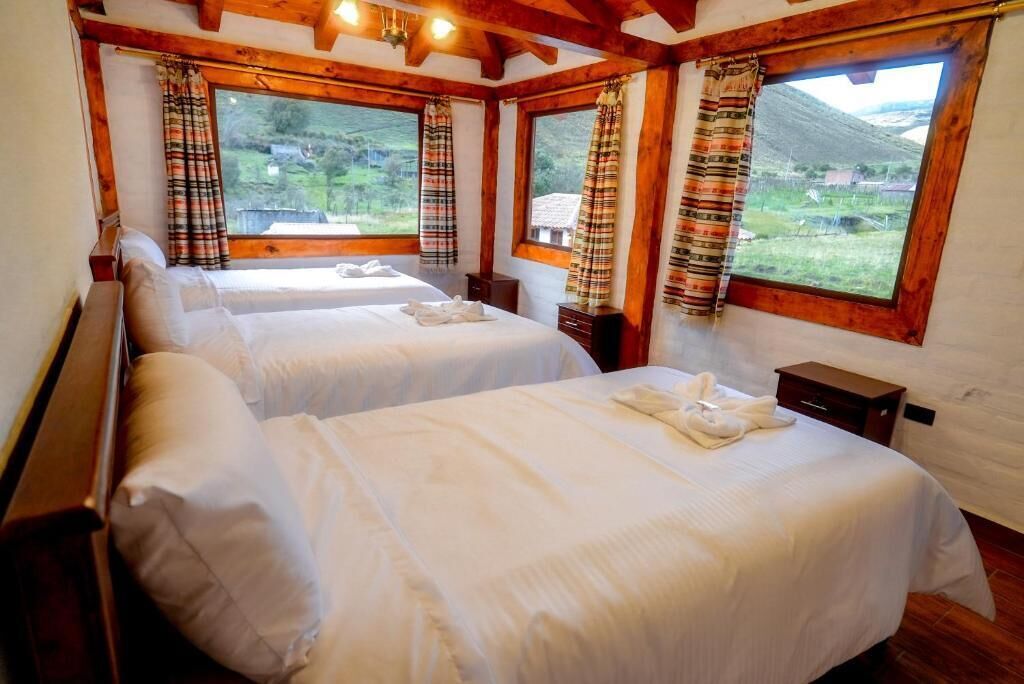 Habitación con dos camas, vigas de madera, ventanas amplias con cortinas y vistas al exterior.