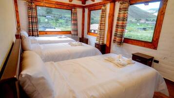 Habitación con dos camas, vigas de madera, ventanas amplias con cortinas y vistas al exterior.