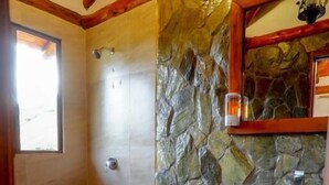 A bathroom with a stone wall, a wooden vanity, a toilet, and a shower.