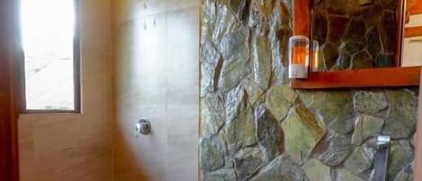 Un baño con pared de piedra, tocador de madera, inodoro y ducha.