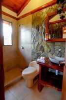 Un baño con pared de piedra, tocador de madera, inodoro y ducha.
