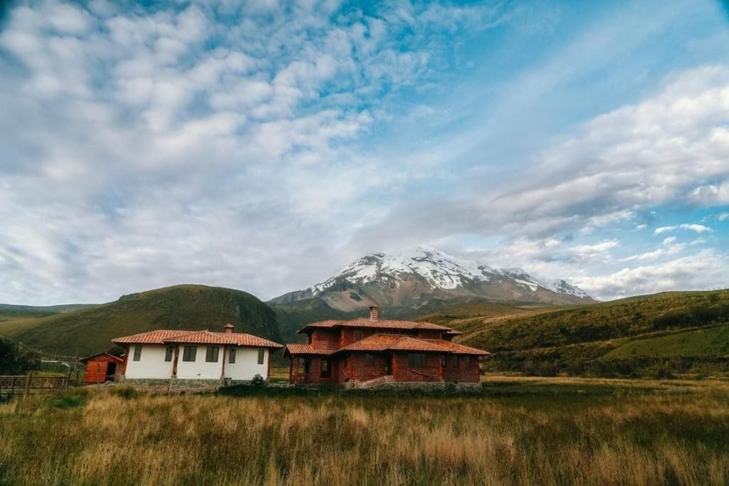 A rural landscape with two traditional houses, a mountain, and a clear sky.