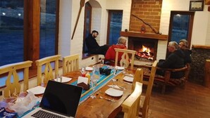 A dining area with wooden furniture, a fireplace, and a view through large windows.