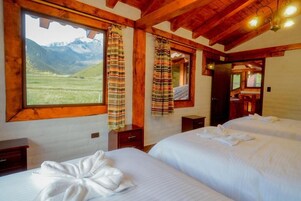 Una habitación con dos camas, vigas de madera, una ventana con cortinas y vistas a montañas.
