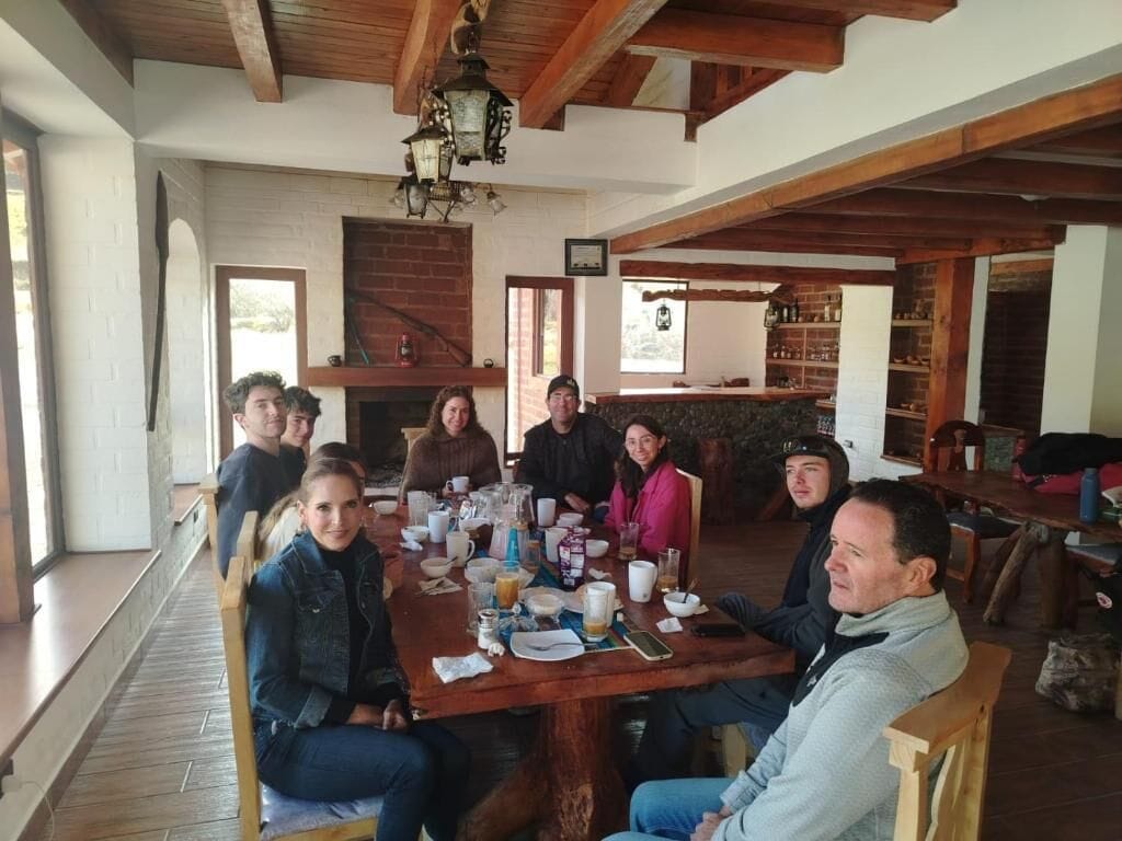 A group of people seated around a wooden table in a room with exposed wooden beams and a brick fireplace.
