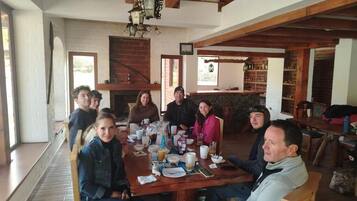 A group of people seated around a wooden table in a room with exposed wooden beams and a brick fireplace.