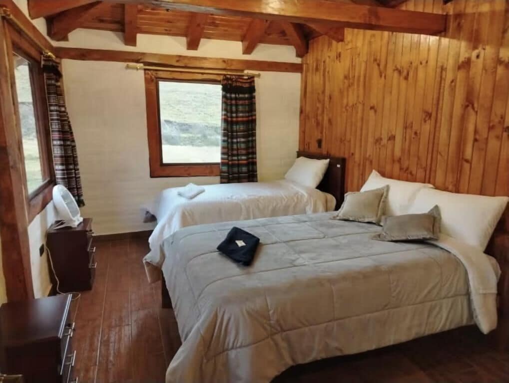 A room with two beds, wooden walls, a window, and a fan.