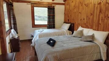 A room with two beds, wooden walls, a window, and a fan.
