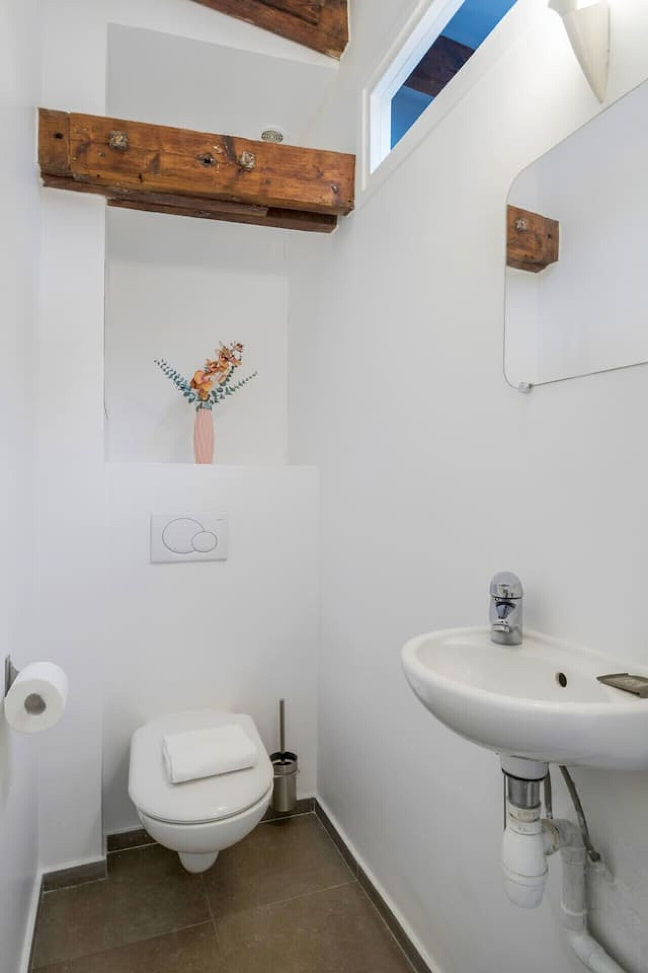 Casa de banho pequena com sanita, lavatório e teto com vigas de madeira.