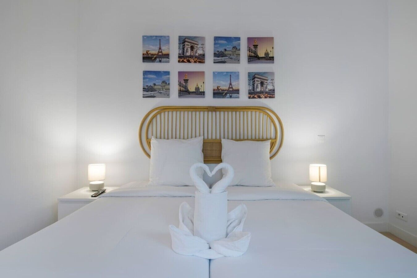 A neatly made bed with white linens, a wooden headboard, and a swan-shaped towel centerpiece.