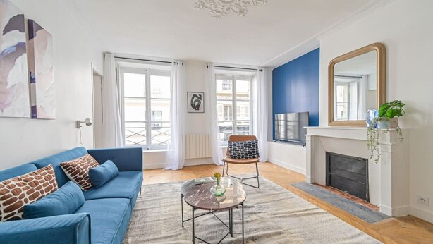 Una sala de estar con un sofá azul, una mesa de centro, una chimenea y un espejo grande.
