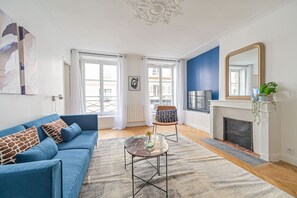 Een woonkamer met een blauwe bank, een salontafel, een open haard en een grote spiegel.