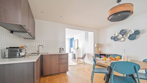 Una cocina moderna con una isla central, un área de comedor con sillas azules y un espacio de sala con un ventanal grande.