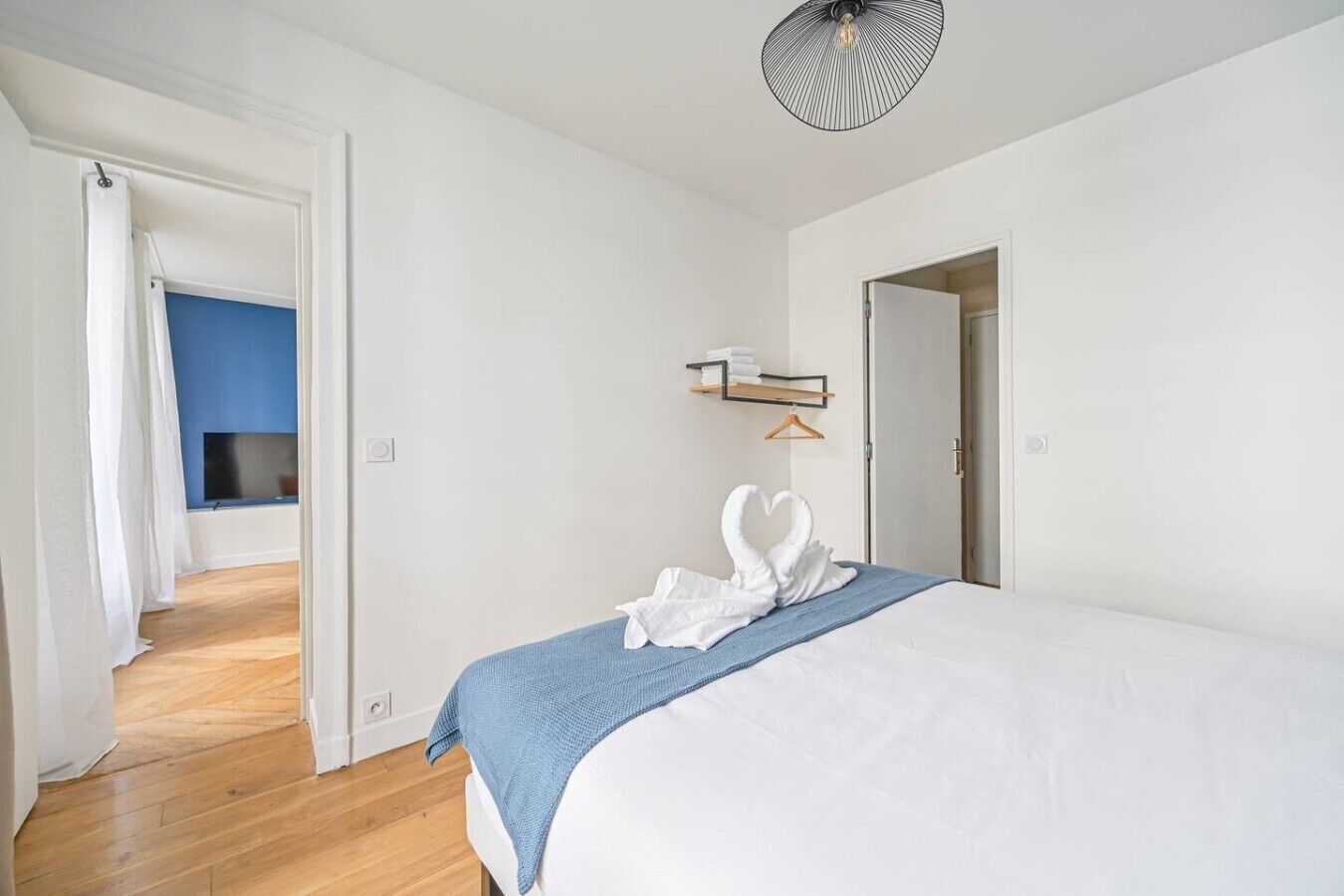 Une chambre d’hôtel avec un lit, un mur bleu, une télévision et une porte donnant sur une autre pièce.