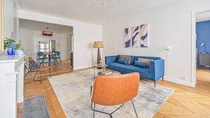 Una sala de estar con un sofá azul, un sillón naranja y un comedor con una mesa y sillas.