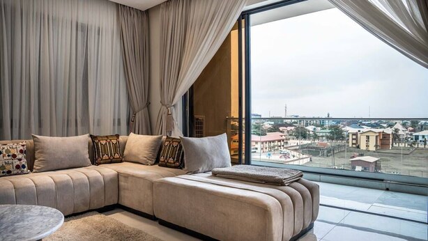 Una sala moderna con un amplio sofá modular, una mesa de centro redonda y vistas de la ciudad a través de grandes ventanales.