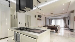 Una cocina moderna con una isla central, un rincón de comedor con sofá y mesa, y un amplio ventanal con cortinas.