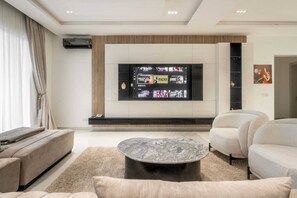 Uma sala de estar moderna com uma televisão de tela plana, uma mesa de centro redonda e um sofá.
