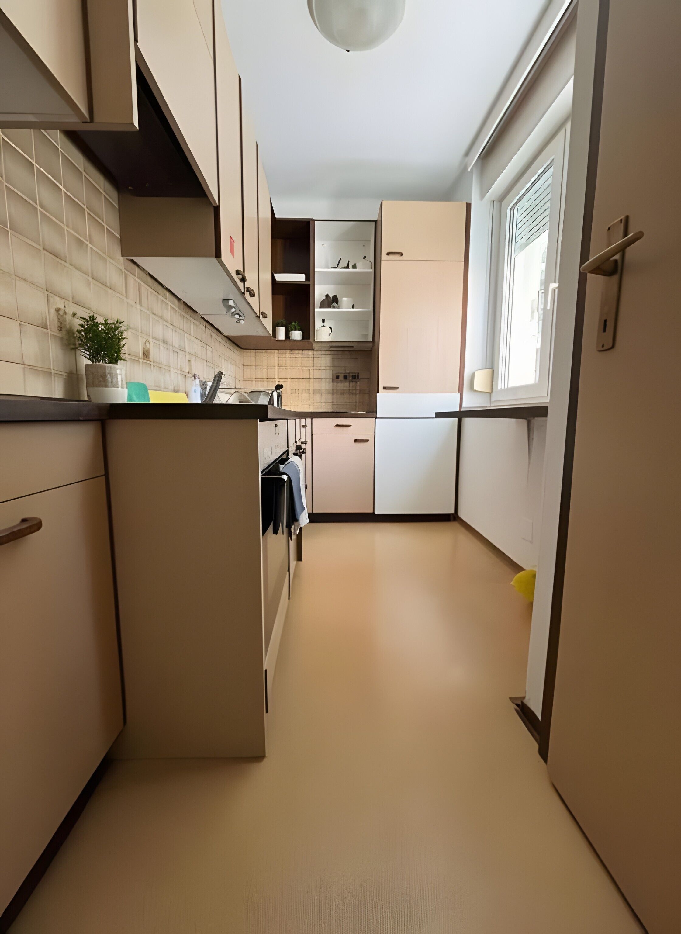 Una cocina estrecha con armarios color beige, salpicadero de azulejos y una ventana con persianas.