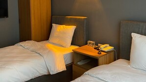 Une chambre d’hôtel avec deux lits, une armoire, une table de chevet avec une lampe et un luminaire fixé au mur.