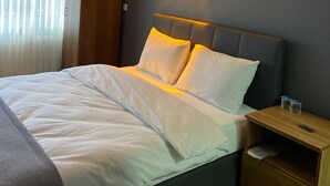 Un lit bien fait, avec du linge de lit blanc, une table de chevet avec une lampe et une armoire.