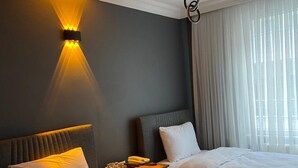 Une chambre d’hôtel avec deux lits, une table de chevet avec un téléphone, une lampe fixée au mur et une fenêtre avec des rideaux.