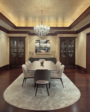 A formal dining room with a large round table, six chairs, a chandelier, and glass-fronted cabinets with cutlery. - Fauzan Country Club: A Private Residential Resort in Atlanta (Marietta)