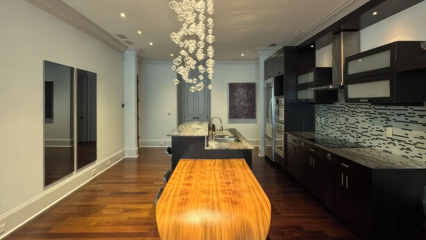 Una cucina moderna con isola centrale, mobili scuri e un lampadario decorativo.