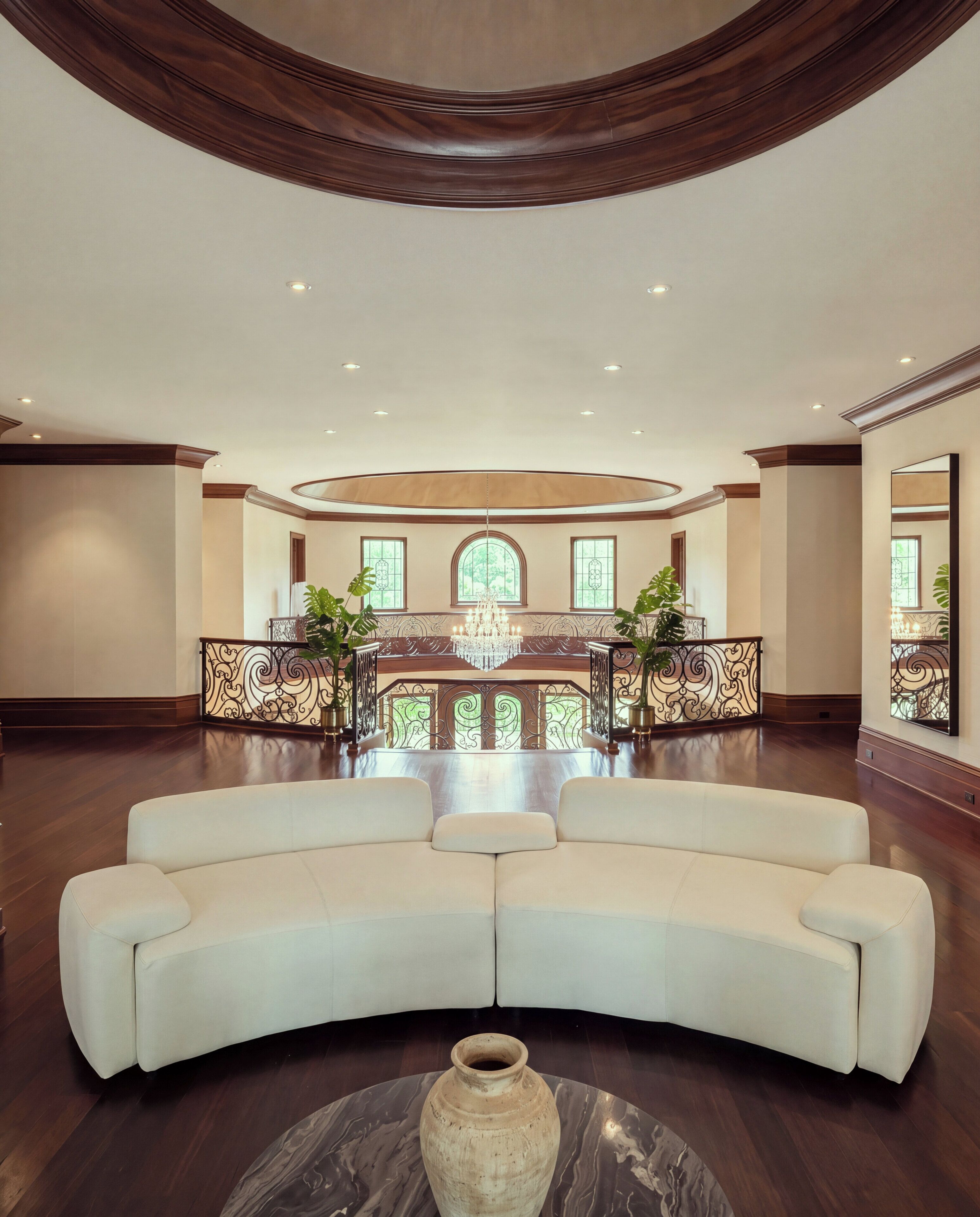 A spacious lobby with a curved white sofa, a chandelier, and a large window.