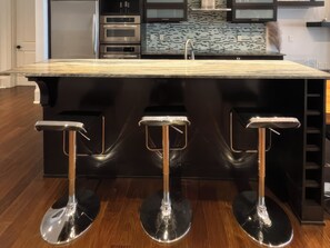 A kitchen with a marble countertop, stainless steel appliances, and three bar stools. - Fauzan Country Club: A Private Residential Resort in Atlanta (Marietta)