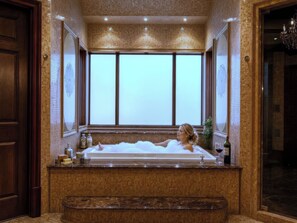 A woman relaxing in a bathtub with a large window behind her, a bottle of wine, and toiletries on the counter. - Fauzan Country Club: A Private Residential Resort in Atlanta (Marietta)
