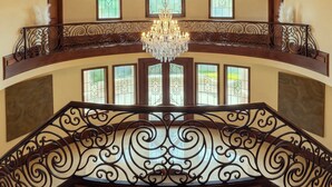 Un'imponente scalinata con ringhiere in metallo decorate e un lampadario, che conduce a un balcone con vetrate ornamentali.