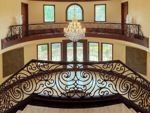 Eine prachtvolle Treppe mit aufwendiger Metallgeländerung und einem Chandelier, das zu einem Balkon mit dekorativen Glasfenstern führt.