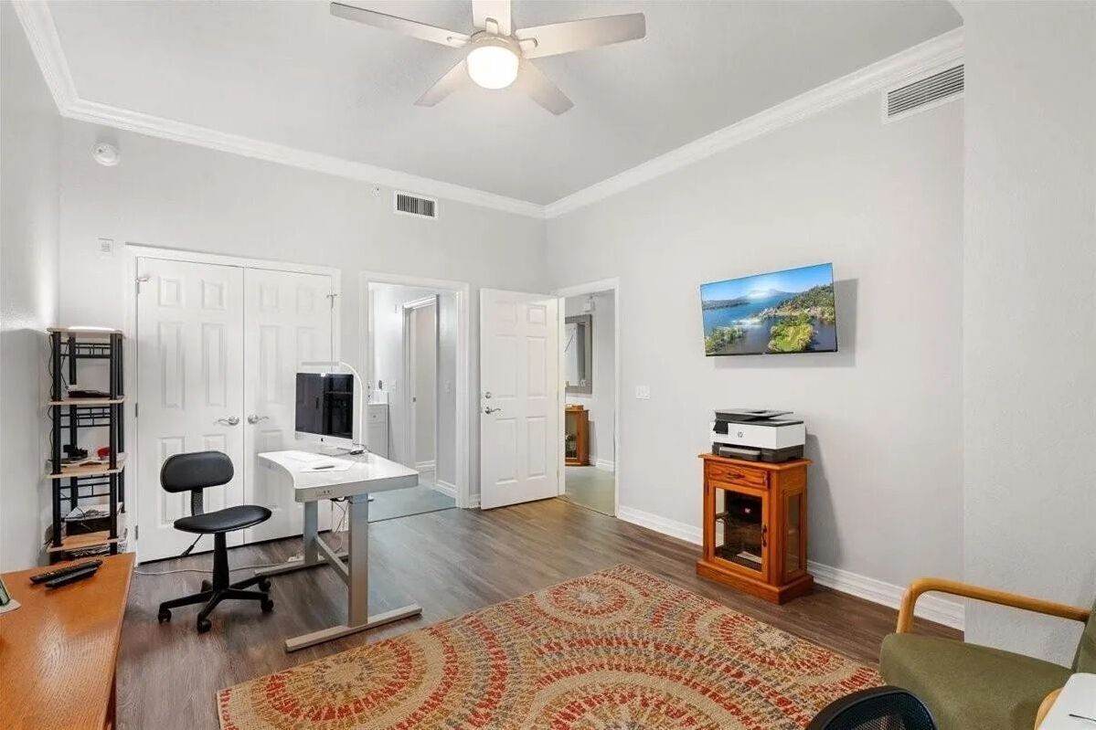 Home office featuring a desk with a computer, wall-mounted TV, and patterned area rug.
