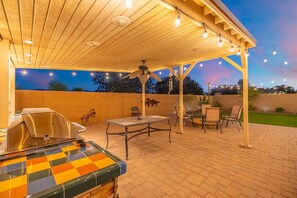 Eine Terrasse im Freien mit einem Grill, einem Tisch, Stühlen und Lichterketten.