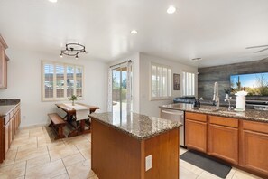 A kitchen with granite countertops, wooden cabinets, a dining table, and a large window. - Spacious 4-Bedroom Home ~ Backyard BBQ Oasis (Phoenix)