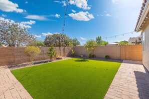Ein Garten mit künstlichem Rasen, Ziegelmauern und Lichterketten.