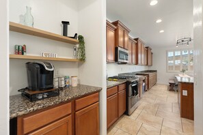 A kitchen with wooden cabinets, granite countertops, a built-in microwave, and a coffee maker. - Spacious 4-Bedroom Home ~ Backyard BBQ Oasis (Phoenix)