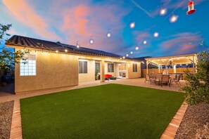 Une maison avec un jardin, une terrasse et des guirlandes lumineuses.
