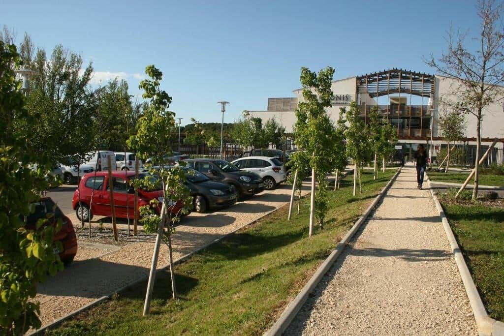 A parking lot with cars, a gravel path, and a building with a modern design in the background.
