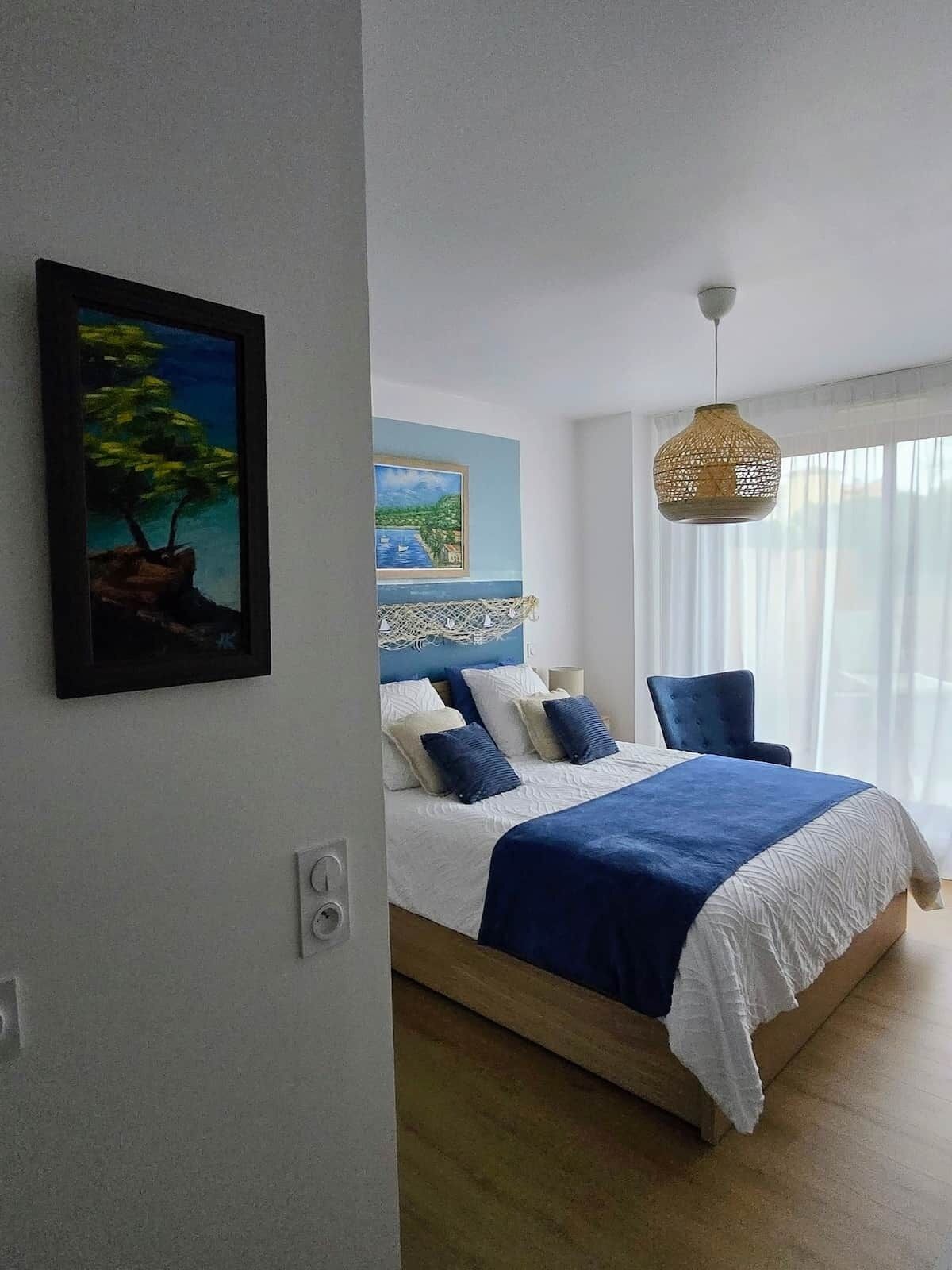A bedroom with a bed, a hanging light fixture, and a painting on the wall.