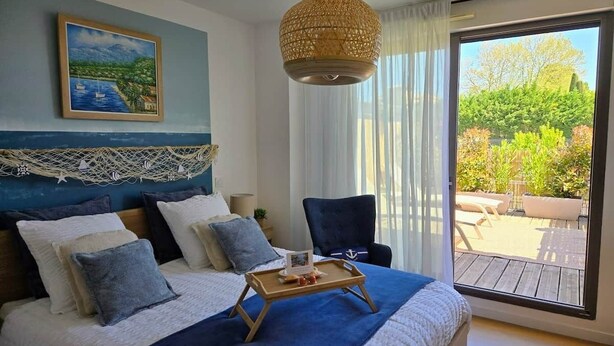 A bedroom with a bed, a chair, a tray with items, a painting, and a view of the outdoors.