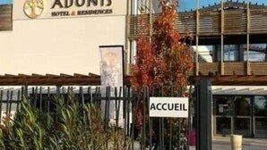 A hotel named Adonis with a modern facade, a sign indicating the entrance, and a pergola structure.