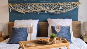 A bed with a blue blanket, two pillows, a wooden tray with glasses and food, and a netted decoration above the bed.