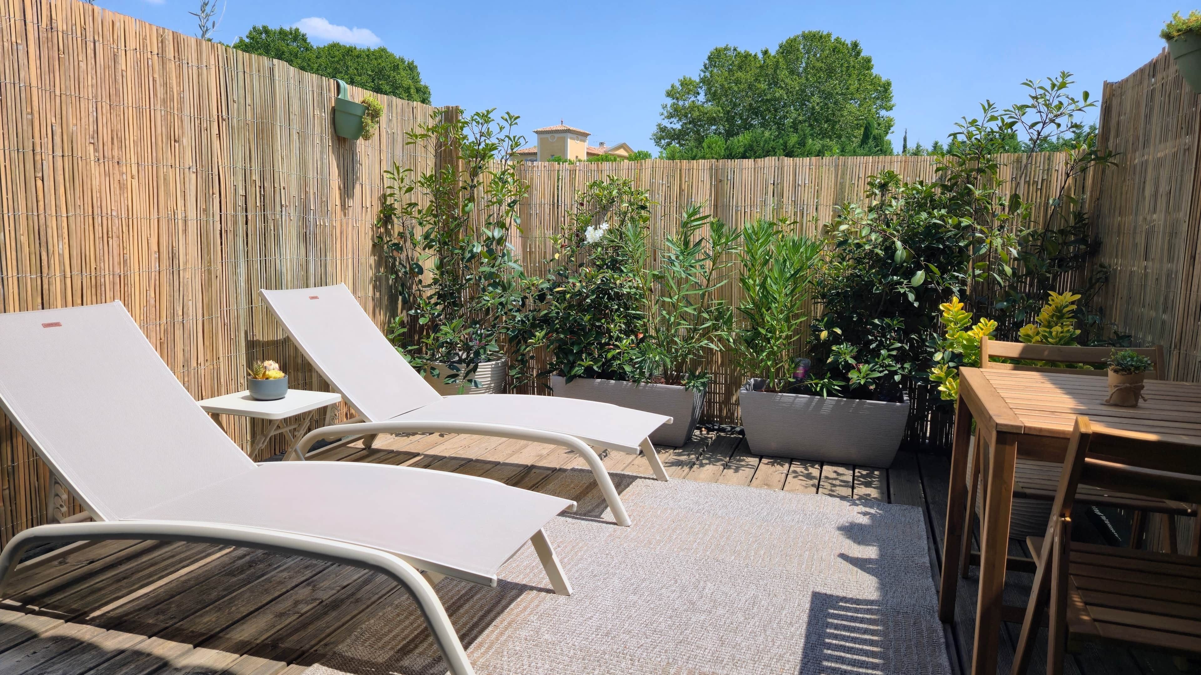 Un patio con dos sillones blancos, una mesa de madera y varias plantas en macetas.